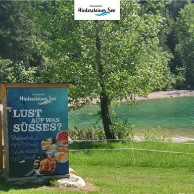 A billboard stands in front of a clear lake, surrounded by trees. The text asks: "Feeling like something sweet?"