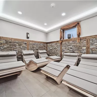 A relaxing wellness area with comfortable wooden loungers. The walls are clad in natural stone and the lighting is soft and inviting.