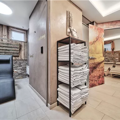 A modern spa with a lounger and neatly stacked towels. The walls are tastefully designed, creating a relaxing atmosphere.