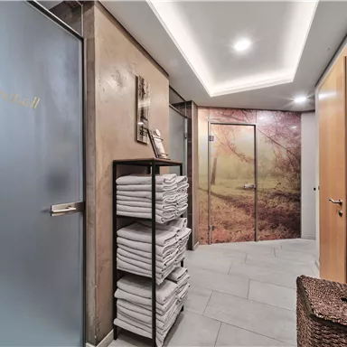 A modern entrance area with a soft lighting design. In the room, towels are on a shelf and a beautiful wall print with an autumnal motif.