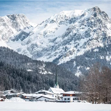 A picturesque winter scene with snow-covered mountains and a small village in the foreground. The landscape exudes tranquility and wintry beauty.