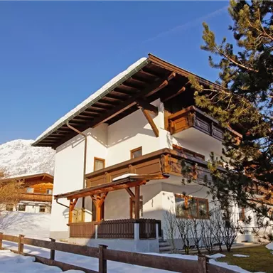 A charming mountain cabin in the snow with traditional wooden architecture. In the background, snow-covered mountains and a clear sky can be seen.