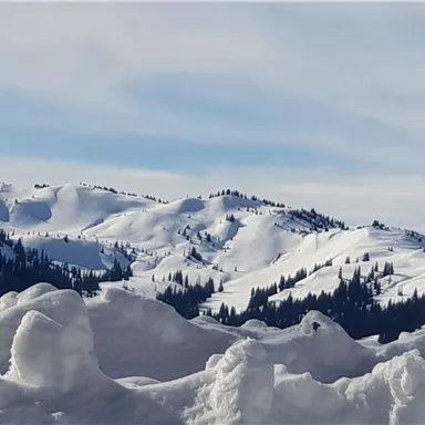 Snow-covered mountains under a clear sky. In the foreground, large snowdrifts can be seen.