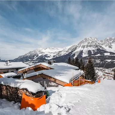 A snowy landscape with cabins and high mountains in the background. The clear sky enhances the wintry atmosphere.