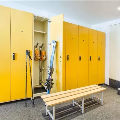 A room with yellow cabinets and a bench. Skis and ski poles are hanging from some cabinets.