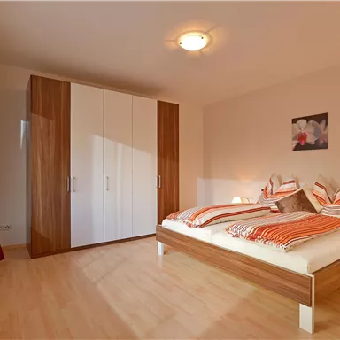 A cozy bedroom with a double bed and striped pillows. A large wardrobe and warm lighting create an inviting atmosphere.