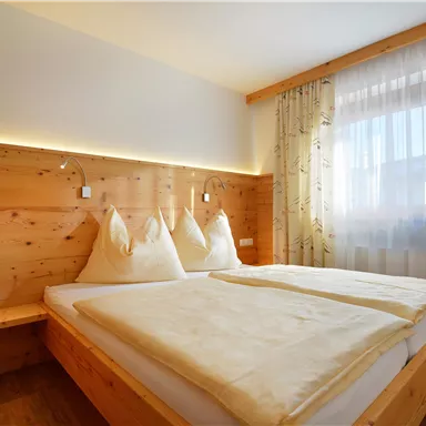 Ein gemütliches Schlafzimmer mit einem Doppelbett und weißen Bettwäsche. Die Wände sind aus hellem Holz, und das Fenster lässt viel Tageslicht herein.