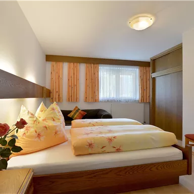 Ein gemütliches Schlafzimmer mit zwei Betten und weichen Kopfkissen. Es gibt eine Blumenvase und einen Stuhl, die für eine einladende Atmosphäre sorgen.