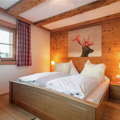 Ein gemütliches Schlafzimmer mit Holzverkleidung und einem großen Fenster. Zwei Betten mit flauschigen Kissen und einer stilvollen Wanddekoration sind zu sehen.