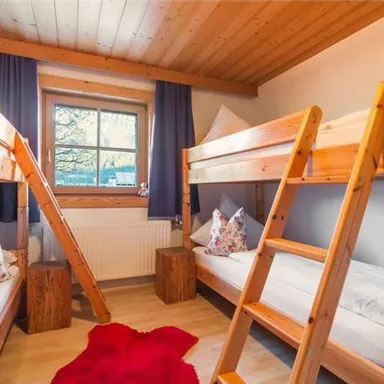 Ein gemütlicher Schlafraum mit zwei Etagenbetten aus Holz. Große Fenster sorgen für viel Licht und die Dekoration ist freundlich und einladend.