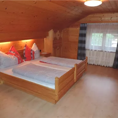Ein gemütliches Schlafzimmer mit Holzwänden und einem großen Doppelbett. Die Fenster lassen viel Tageslicht herein und die Dekoration ist einfach und einladend.