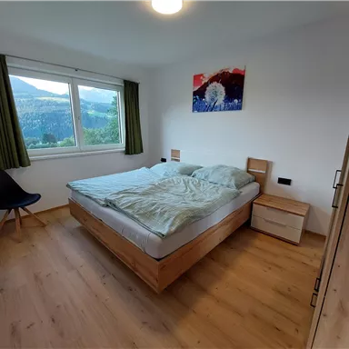 Ein modernes Schlafzimmer mit einem Doppelbett und Holzfußboden. Große Fenster bieten einen Blick auf die Berge und die Dekoration ist schlicht und einladend.