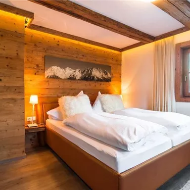 Ein gemütliches Schlafzimmer mit Holzwänden und einem großen Bett. Große Fenster lassen viel Tageslicht hinein und schaffen eine einladende Atmosphäre.