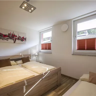 A cozy bedroom with a double bed and a single bed. Bright walls and large windows create a pleasant atmosphere.