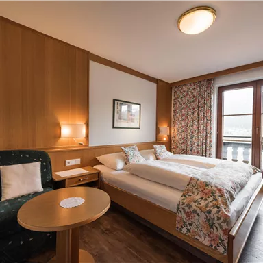 A comfortable hotel room with two beds and cozy furnishings. Large windows offer a view outside.