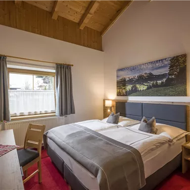 Ein gemütliches Schlafzimmer mit zwei Betten und einem Holzdach. Das Zimmer ist hell und freundlich eingerichtet, mit einem schönen Landschaftsbild an der Wand.