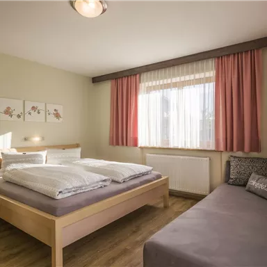 A bright bedroom with a double bed and a cozy sofa. Large windows let in plenty of daylight and give the room an inviting atmosphere.