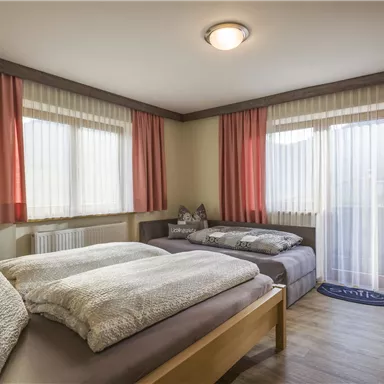 A cozy bedroom with two beds and large windows. The curtains are in soft colors and let in plenty of light.