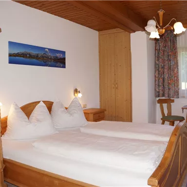 Ein gemütliches Schlafzimmer mit zwei Einzelbetten und einem holzgetäfelten Schrank. Große Fenster lassen viel Licht herein und sorgen für eine einladende Atmosphäre.