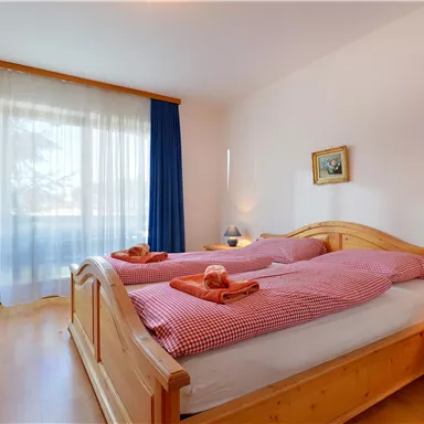 A cozy bedroom with two single beds and wooden furniture. Curtains let daylight in and give the room a bright atmosphere.