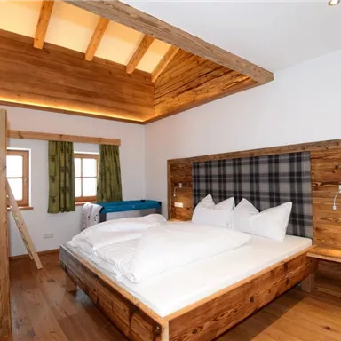 Ein gemütliches Schlafzimmer mit einem Doppelbett und einem Etagenbett. Die Holzmöbel und der natürliche Lichtfall sorgen für eine einladende Atmosphäre.