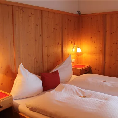 Ein gemütliches Schlafzimmer mit zwei Einzelbetten und Holzwänden. An den Wänden befinden sich Lichtquellen, die eine warme Atmosphäre schaffen.