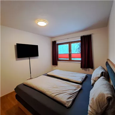 Ein gemütliches Schlafzimmer mit zwei Betten und einem Fernseher. Das Fenster bietet einen Blick auf die winterliche Landschaft.
