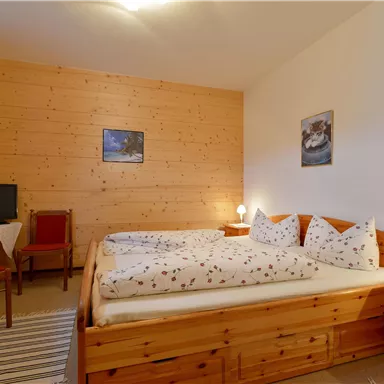 Ein gemütliches Schlafzimmer mit Holzverkleidung und einem Doppelbett. Es gibt einen Tisch, Stühle und einen Fernseher in der Ecke.