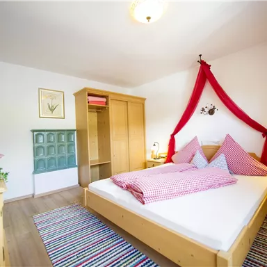 A cozy bedroom with a double bed and red accents. The walls are painted light and there is a television as well as a wardrobe.