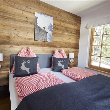 Ein gemütliches Schlafzimmer mit einem Holzpanel-Wand und einem großen Fenster. Das Bett ist mit karierten Kissen und einer Decke dekoriert.