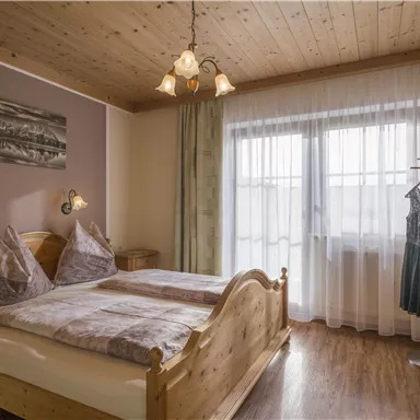 A cozy bedroom with two wooden beds and a large window. The walls are painted in gentle colors and a wardrobe stands in the room.
