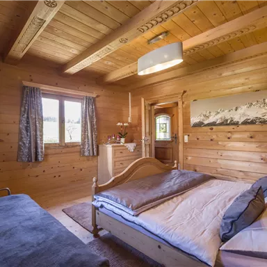 Ein gemütliches Schlafzimmer aus Holz mit einem großen Bett und einem Blick auf die Natur. Die Einrichtung ist rustikal und einladend, mit einer warmen Atmosphäre.