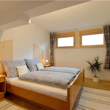 Ein helles Schlafzimmer mit zwei Betten und gemütlicher Bettwäsche. Große Fenster sorgen für naturlisches Licht und eine frische Atmosphäre.