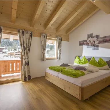 Ein gemütliches Schlafzimmer mit einem großen Bett und grünen Kissen. Durch die Fenster ist eine schöne Aussicht auf die Berge sichtbar.