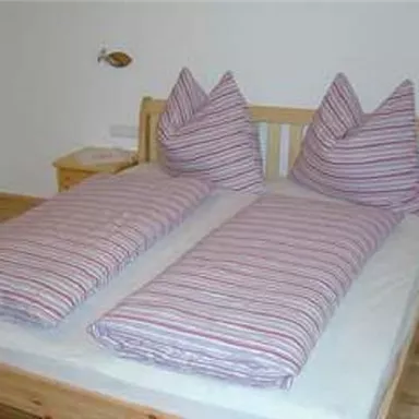 A simple bedroom with a double bed and striped bedcovers. The pillows are high and pointed, and the floor is wooden.