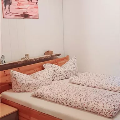 A cozy bedroom with a wooden bed and matching pillows. On the wall hangs a picture of camels in the desert.