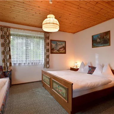 Ein gemütliches Zimmer mit Holzboden und Holzwänden. Es gibt zwei Betten, Tischlampen und Fenster mit Vorhängen.