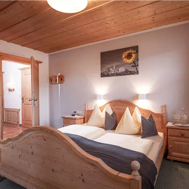 A cozy bedroom with a double bed and wooden paneling. A picture of sunflowers hangs on the wall, and there is soft lighting.