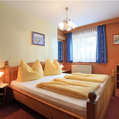 Ein gemütliches Schlafzimmer mit einem Doppelbett und gelben Decken. Helle Fenster und Holzverkleidung verleihen dem Raum eine einladende Atmosphäre.