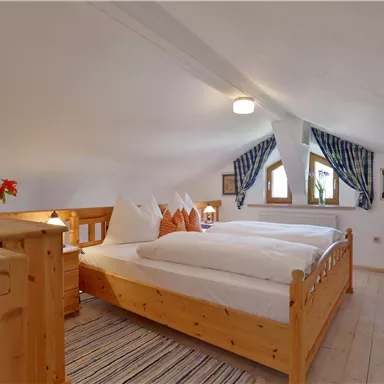 Ein gemütliches Schlafzimmer mit Holzmöbeln und zwei Betten. Die Fenster sind mit karierten Vorhängen dekoriert und es gibt frische Blumen auf dem Nachttisch.