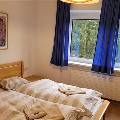 Ein gemütliches Schlafzimmer mit zwei Betten und einem großen Fenster. Die blauen Vorhänge und das Kunstwerk an der Wand sorgen für eine einladende Atmosphäre.