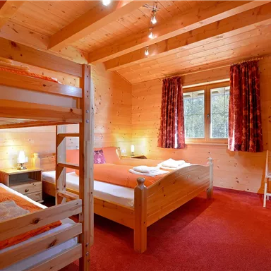 Ein gemütliches Holzzimmer mit zwei Betten und einem Hochbett. Der Raum hat orangefarbene Akzente und große Fenster mit Blick auf die Natur.