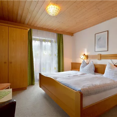 Ein gemütliches Schlafzimmer mit zwei Betten und hellem Holzdekor. Großzügige Fenster lassen viel Licht herein und verleihen dem Raum eine einladende Atmosphäre.