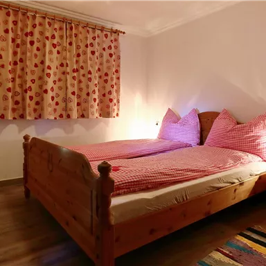 Ein gemütliches Schlafzimmer mit einem Holzbetten und karierten Bettwäsche. Vor dem Fenster hängt ein Vorhang mit roten Punkten.