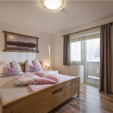A cozy bedroom with a double bed and modern wooden furniture. Large windows provide plenty of daylight and a view outside.