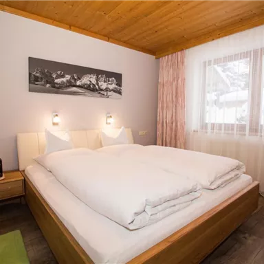A cozy bedroom with a double bed and natural wood decor. Large windows let in plenty of light and offer a view of the snowy landscape.