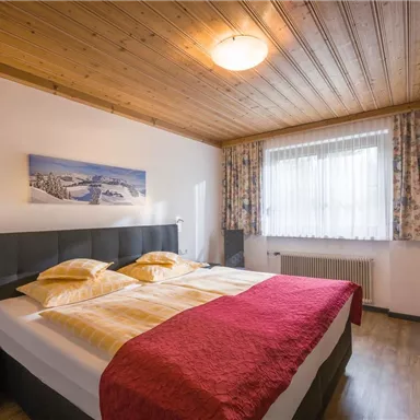 Ein gemütliches Schlafzimmer mit einem Doppelbett und weißer Bettwäsche. Die Wände sind hell, und ein großes Fenster sorgt für viel Tageslicht.
