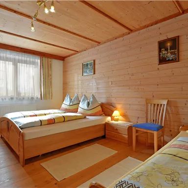 Ein gemütliches Schlafzimmer mit zwei Betten aus Holz. Die Wände sind aus Holz, und es gibt große Fenster für viel Tageslicht.