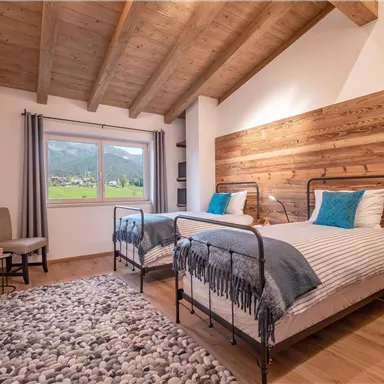 Ein gemütliches Schlafzimmer mit zwei Betten und einem Holzwandpaneel. Große Fenster bieten einen Blick auf die Natur und einen modernen, einladenden Stil.