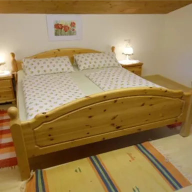 Ein gemütliches Schlafzimmer mit einem großen Holzbett und bequemen Kissen. Zwei Nachttische mit Lampen und Teppichen sorgen für eine einladende Atmosphäre.